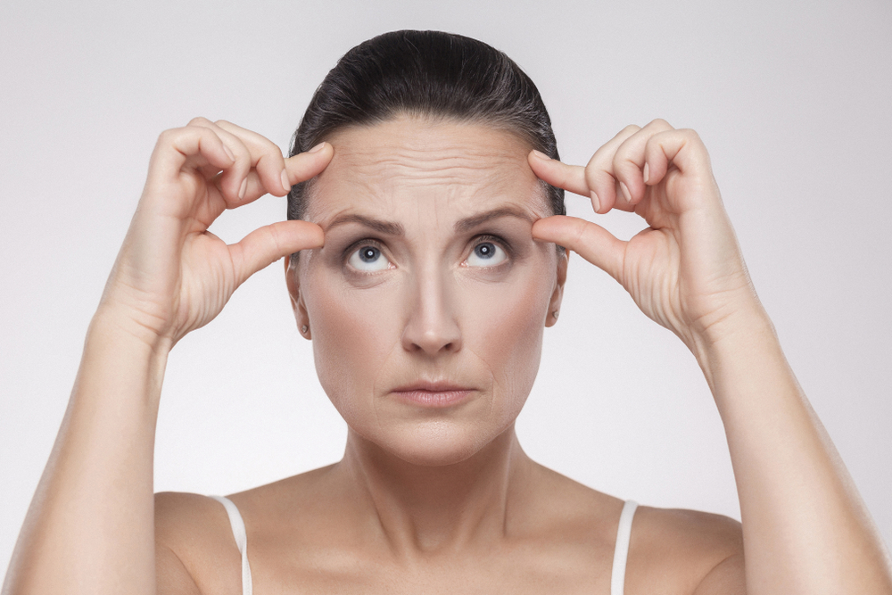 a middle-aged woman pinching the skin above her brows in concern because they have wrinkles