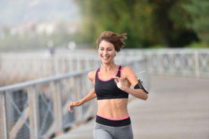 A Woman is jogging along the waterfront. She is smiling.