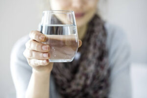 A woman holds up a glass of water. Her face is out of frame.